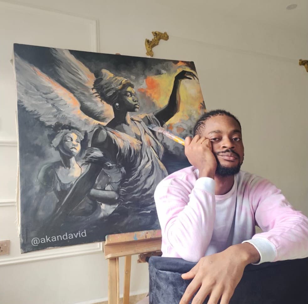Akan David in art studio next to large angel painting